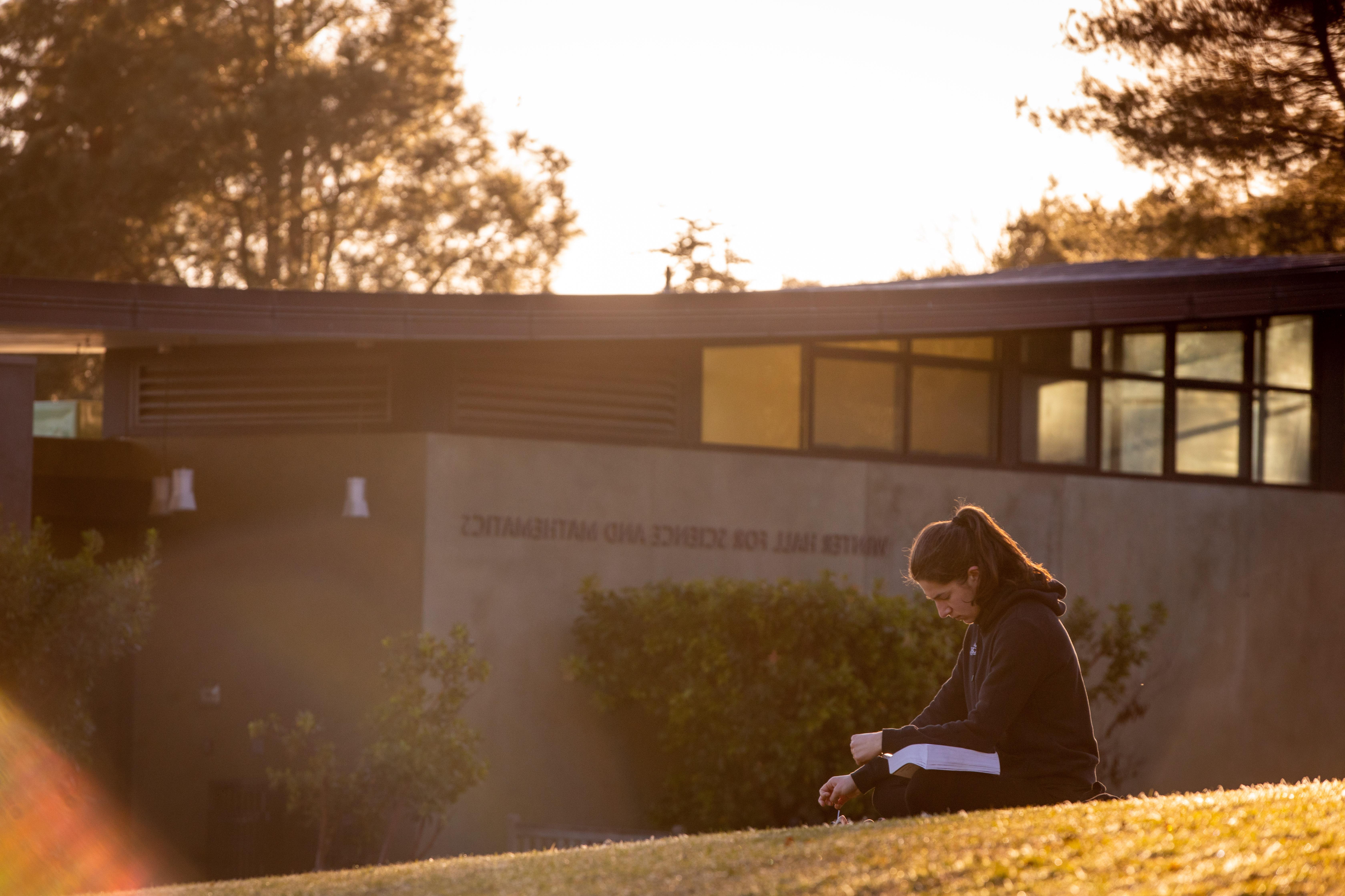 student sitting on grass in front of math building